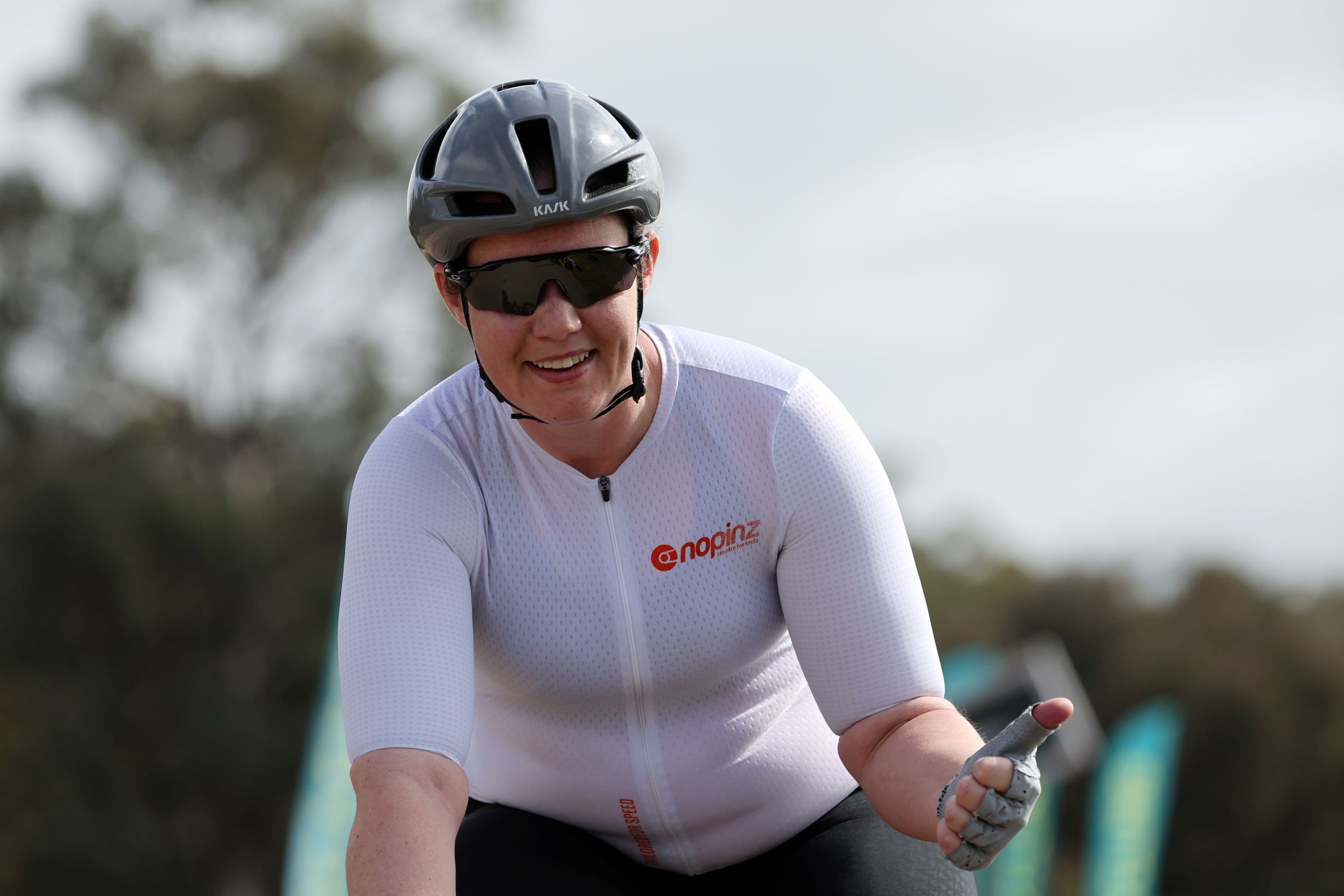 A female competitive road racing cyclist in a Masters age cataegory smiles and gives a thumbs up after finishing a race